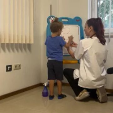 Дете с диспраксия извършва ежедневни задачи с помощта на терапевт, упражнявайки умения за самостоятелност.