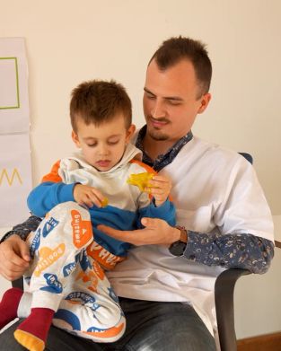 Дете участва в сензорна интеграциионна терапия за деца, използвайки интерактивни материали като пластелин, топки, текстури и светлинни елементи за развитие на сетивата, координация и внимание в модерен детски център.